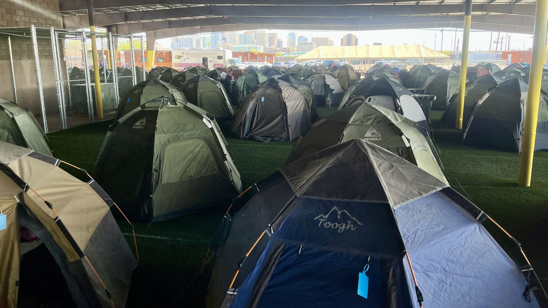 Camping tents under an awning with a city skyline in the background. 