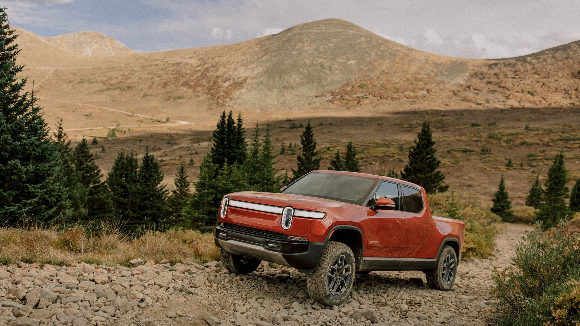 Image of a red Rivian electric pickup truck in a dusty mountain environment