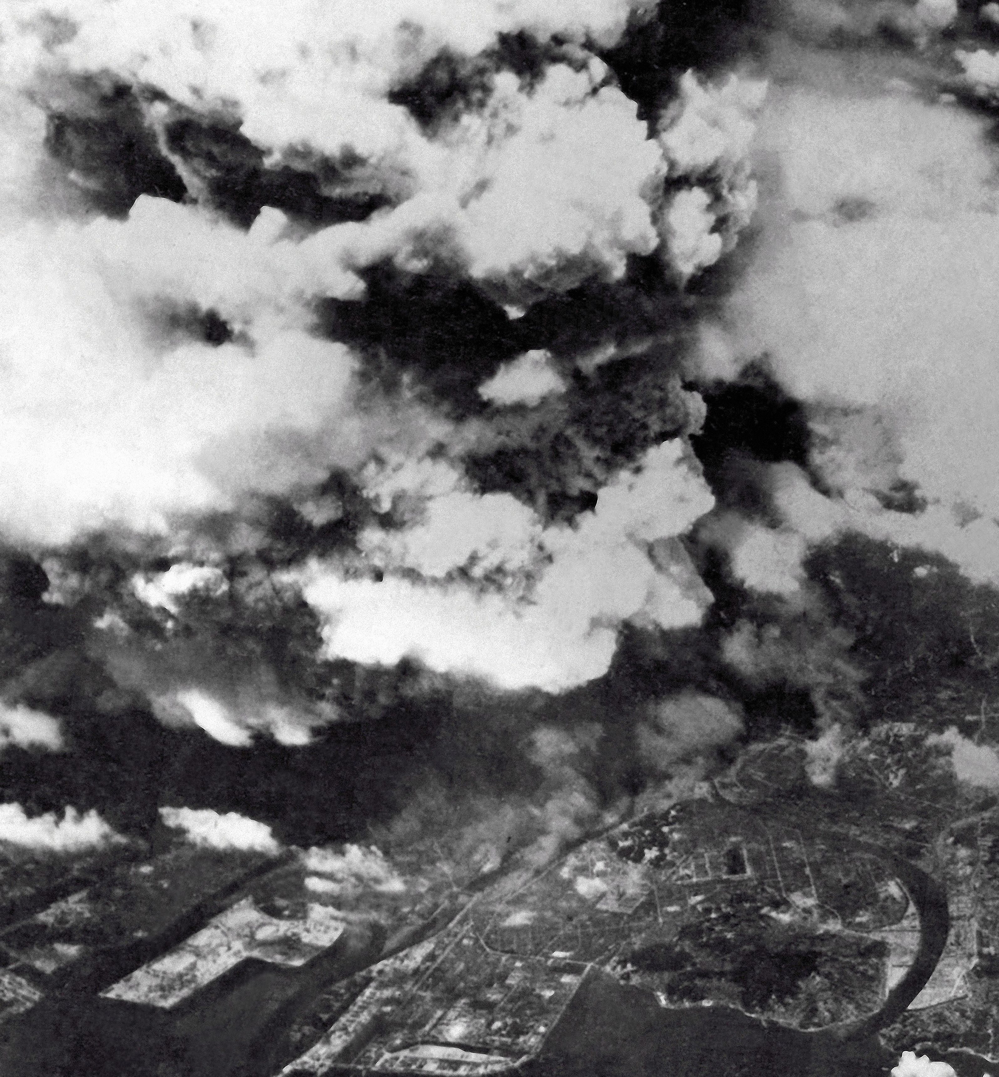 Black and white aerial photo showing extensive smoke and clouds over a city, indicating heavy bombing or fire damage during a wartime event.
