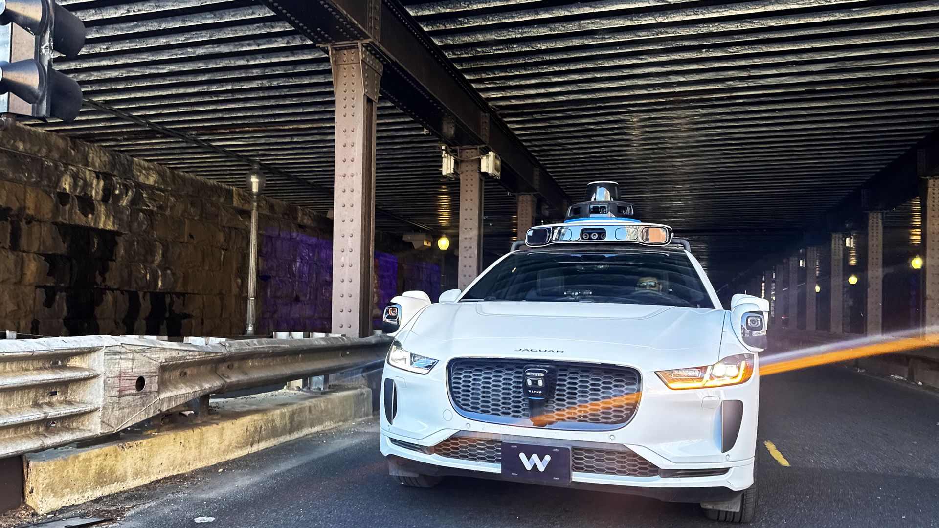 A Waymo Jaguar SUV driving on K Street NE under an overpass