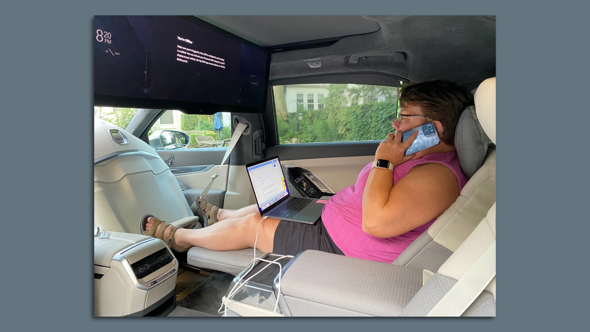 Photo of the author reclining in a BMW i7 as she balances a laptop and mobile phone.