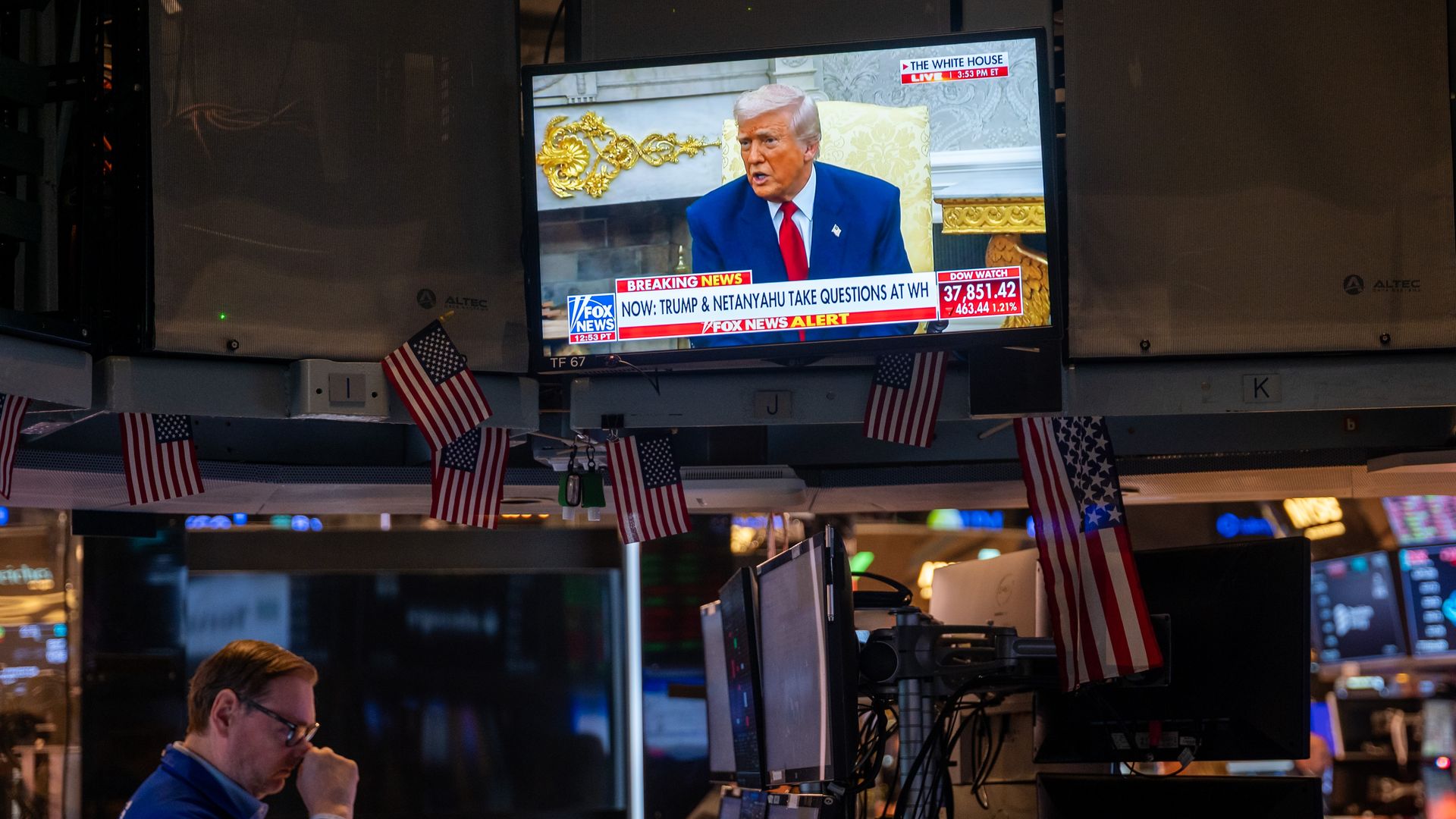A trading floor with a tv showing President Trump abpve it