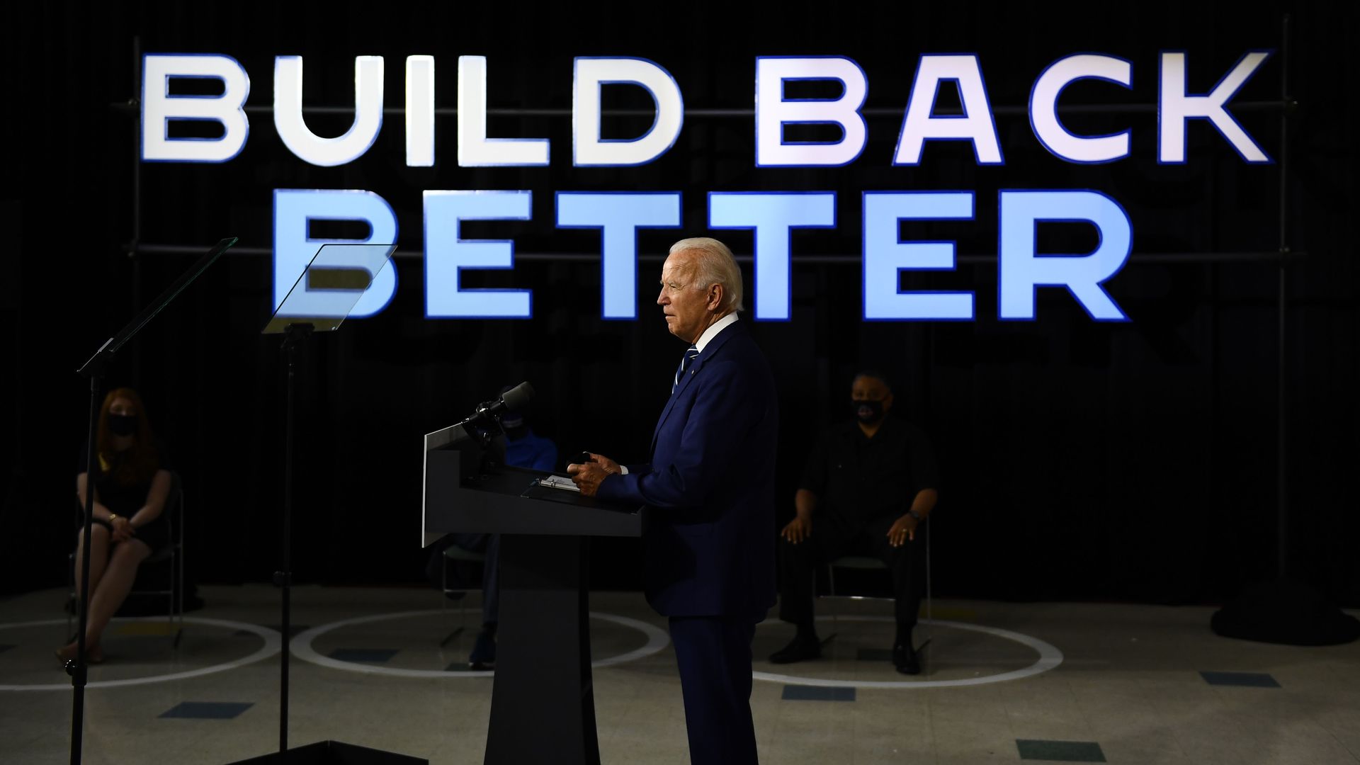 Photo of President Biden speaking in front of a large graphic of the words "Build Back Better"