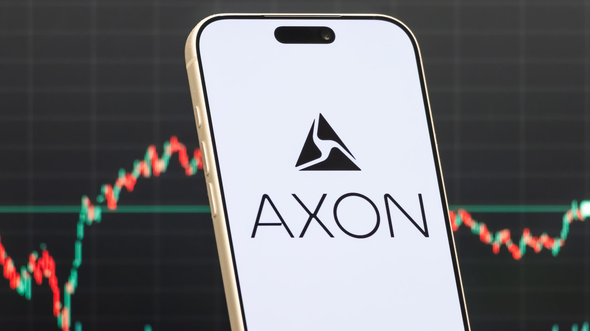 A white smartphone screen showing the word "AXON" and a triangular logo, with a red and green stock graph on a black background. 