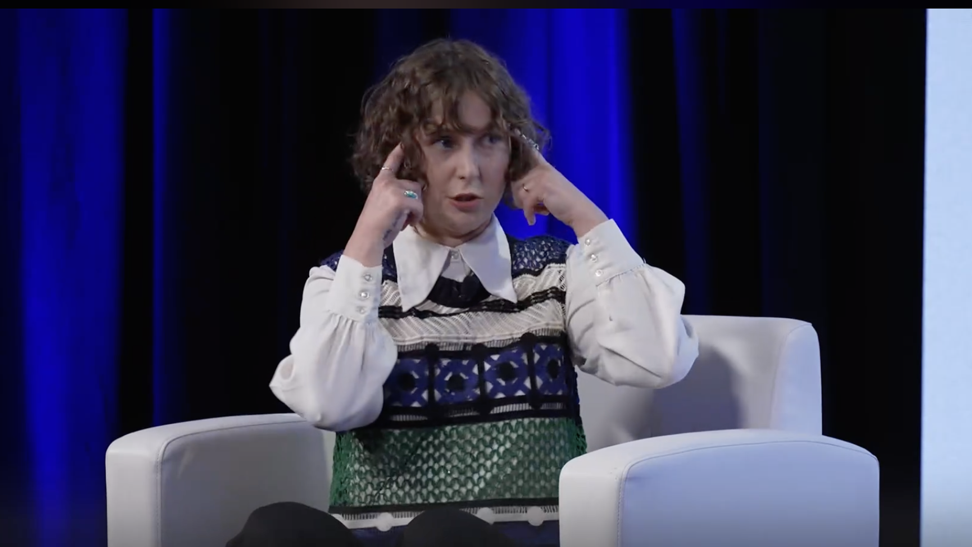 Woman in a chair pointing at her head