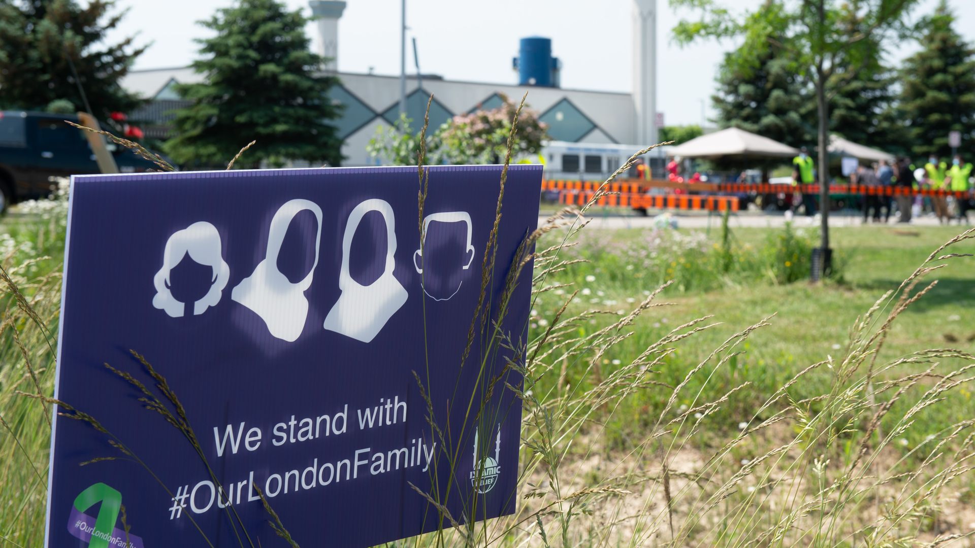 Photo of a sign in the grass that depicts four faceless people and the words "We stand with #OurLondonFamily"