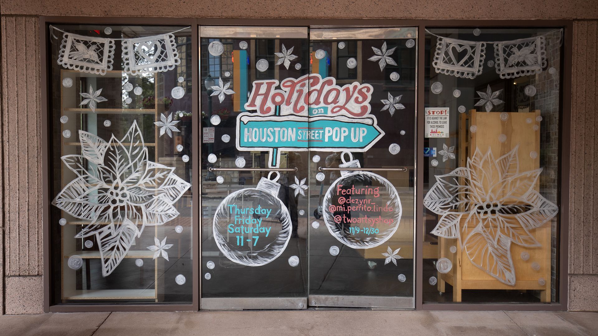A three-pane glass storefront with holiday-themed decorations painted on the windows. 