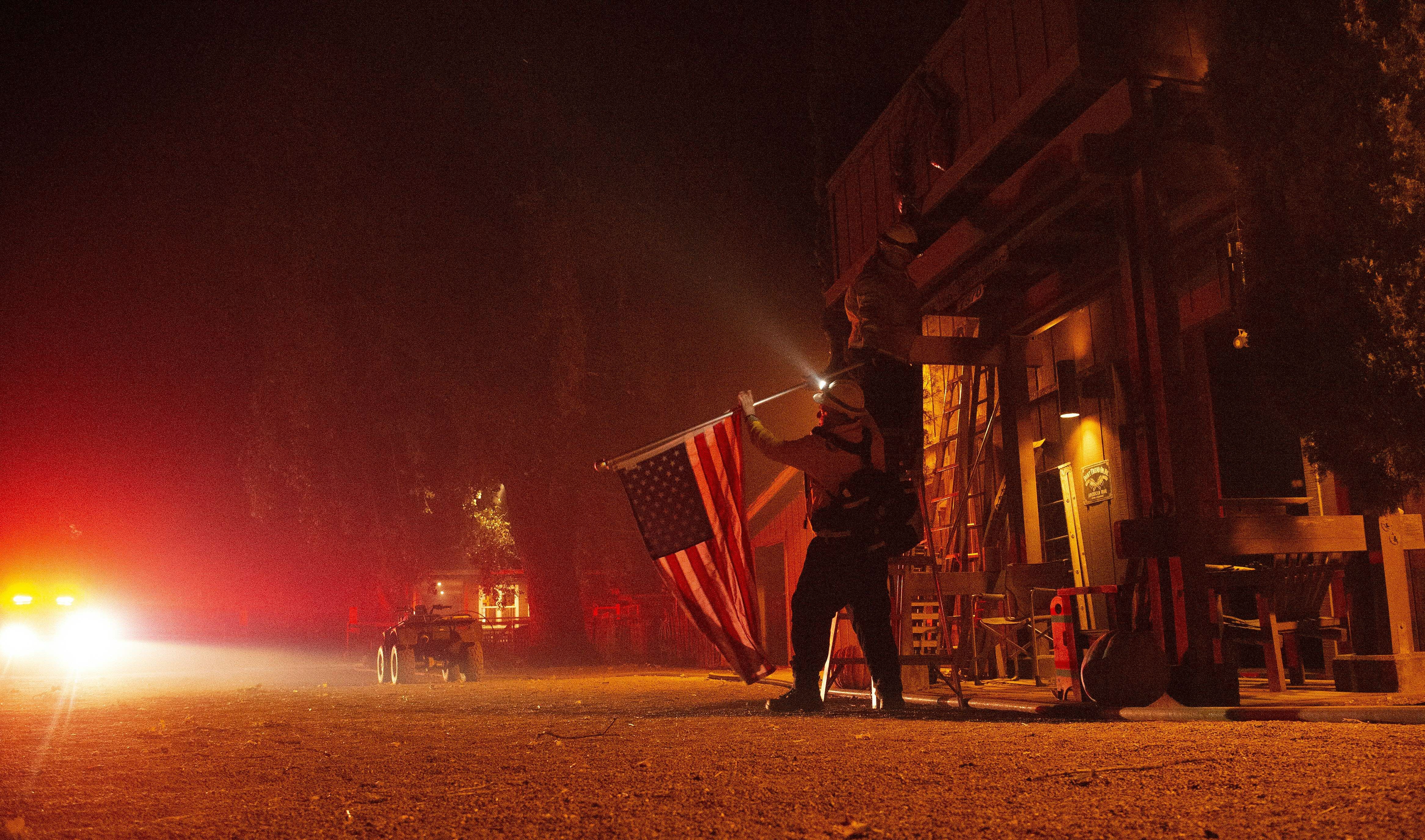 Firefighters remove a US flag from a property as flames race into the area during the Kincade fire in Healdsburg