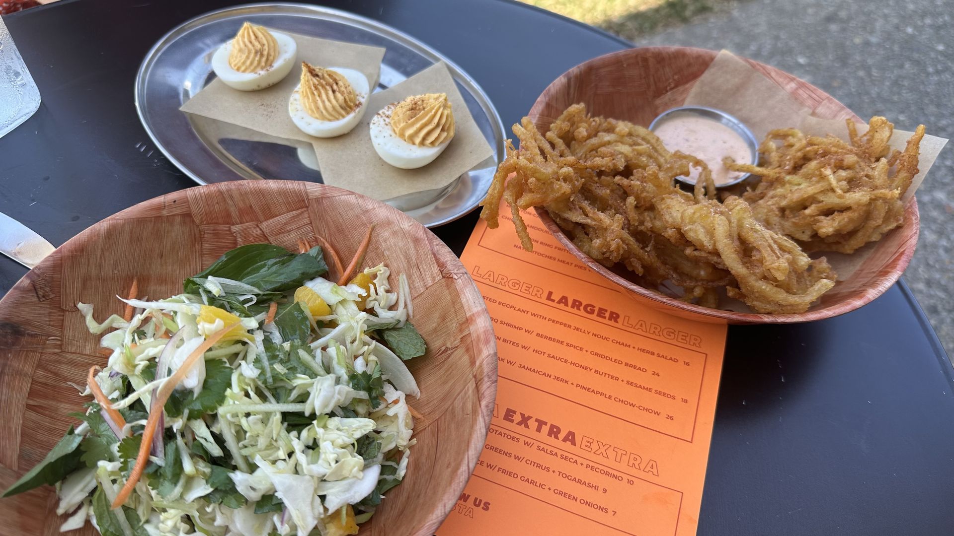 A black tabletop is set with plates of salad, deviled eggs and onion fritters.