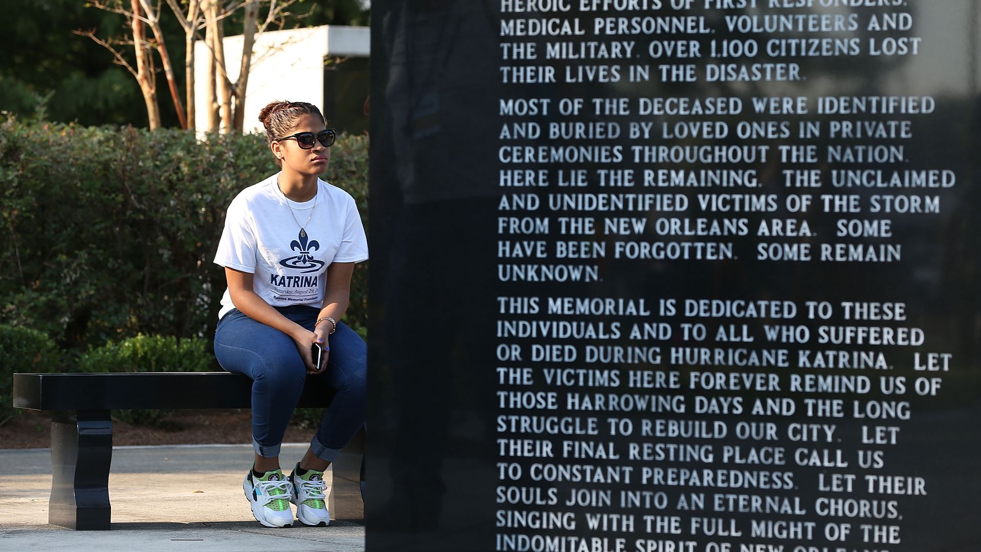 Image shows a memorial wall with woman sitting on a bench.