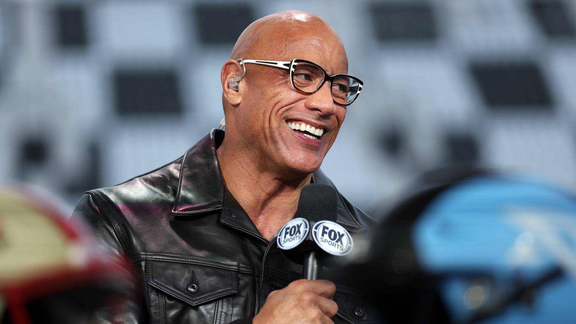 Dwayne The Rock Johnson smiles while holding a microphone