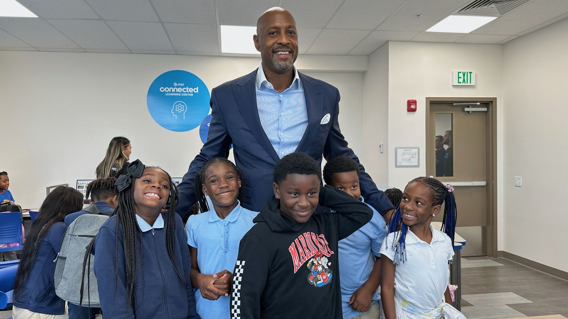 Five kids smile while standing with Miami Heat star Alonzo Mourning who wears a blue suit. 