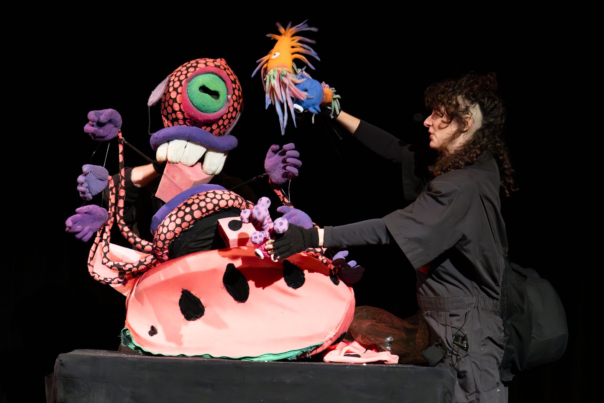 A puppeteer performs with brightly colored monster puppets during an Ow wOw mEoW show, featuring oversized eyes, tentacles and whimsical creatures.