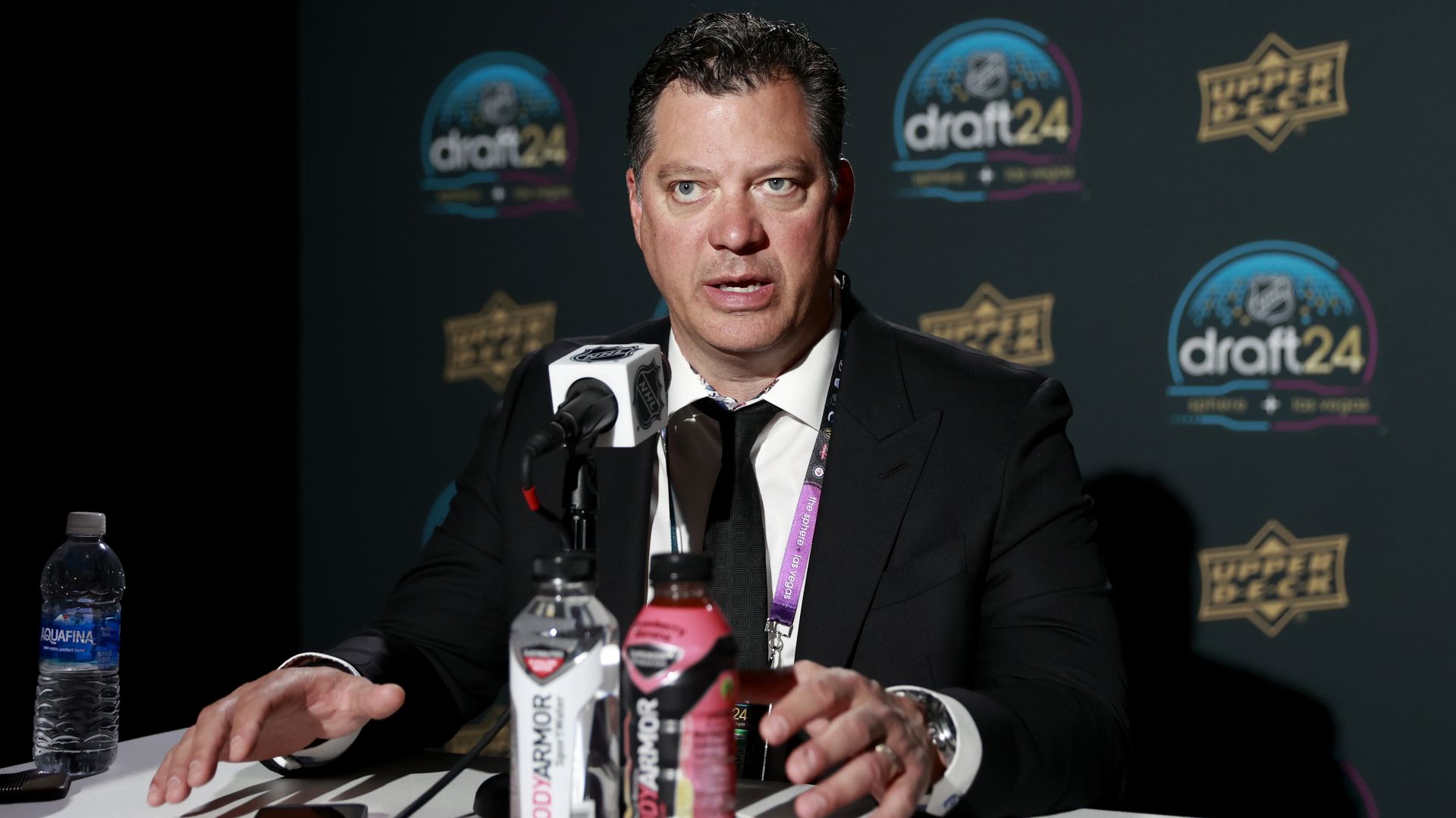 Minnesota Wild GM Bill Guerin speaks at a press conference wearing a dark suit and pinkish lanyard