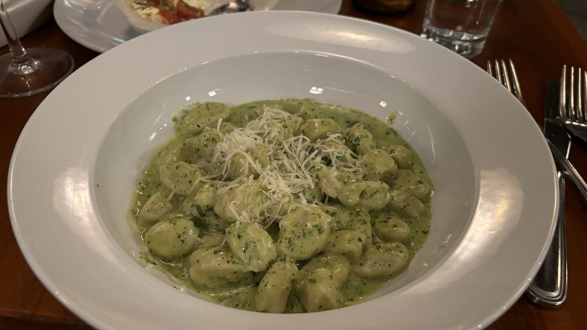 A white plate with pesto gnocchi in the center