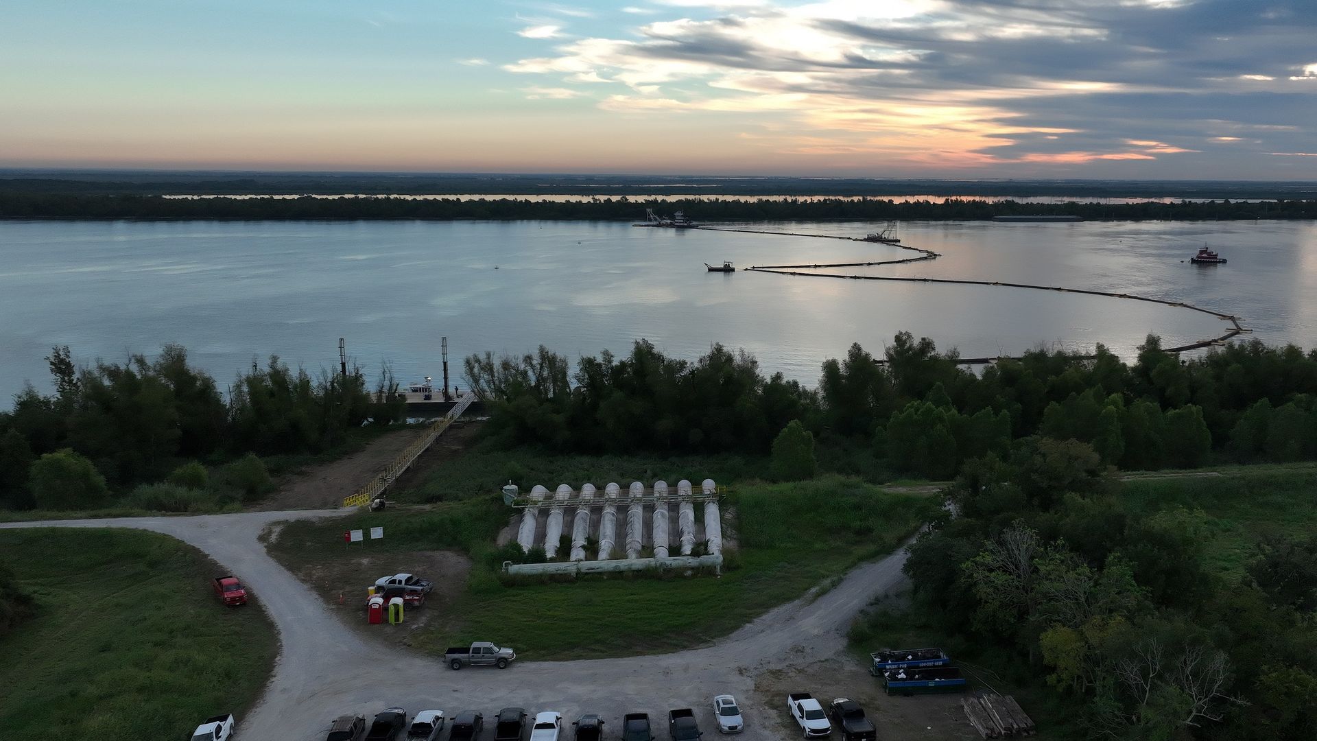 An aerial view of the Mississippi River at dusk. The river is seen with booms stretched across it.