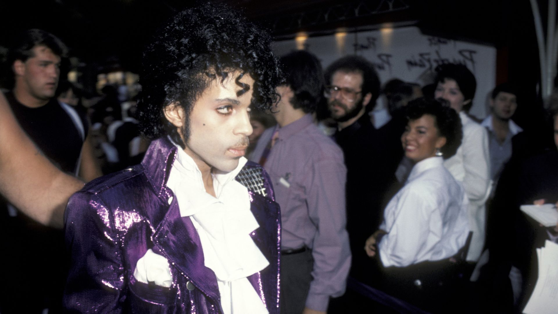 Musical artist Prince wearing a white cravat and a shiny purple jacket photographed at a film premiere