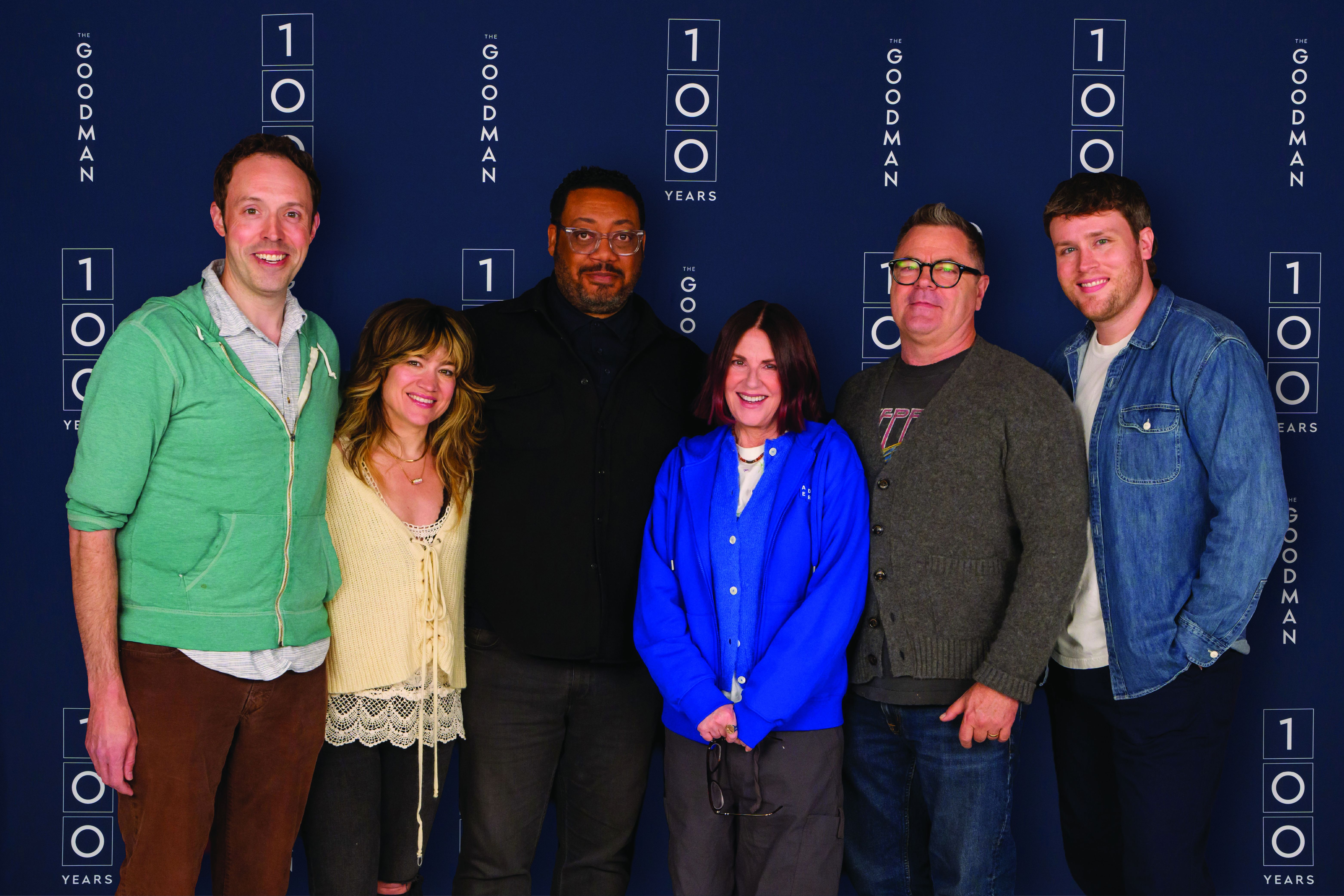 Photo of a group of people posing for a picture in front of a backdrop that says 100 Goodman.