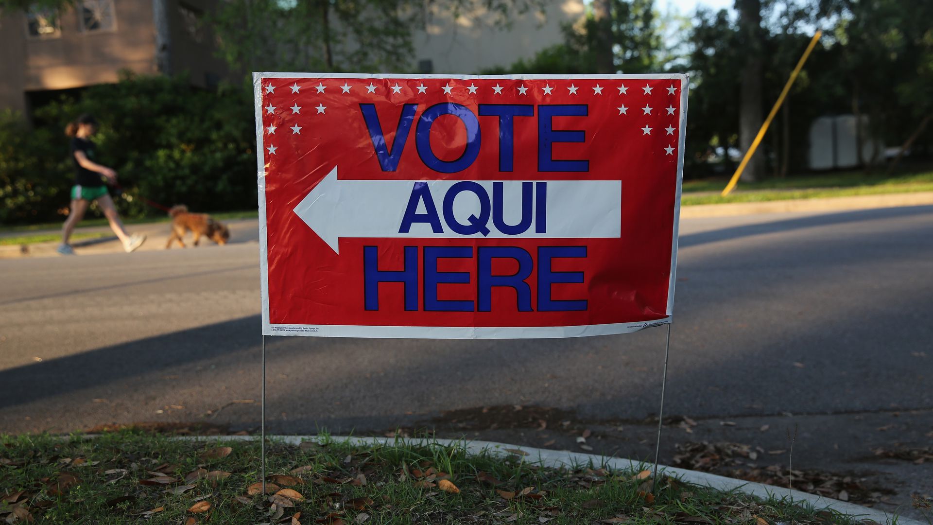 In this image, a sign reads "Vote Aqui Here" on a lawn in a neighborhood.