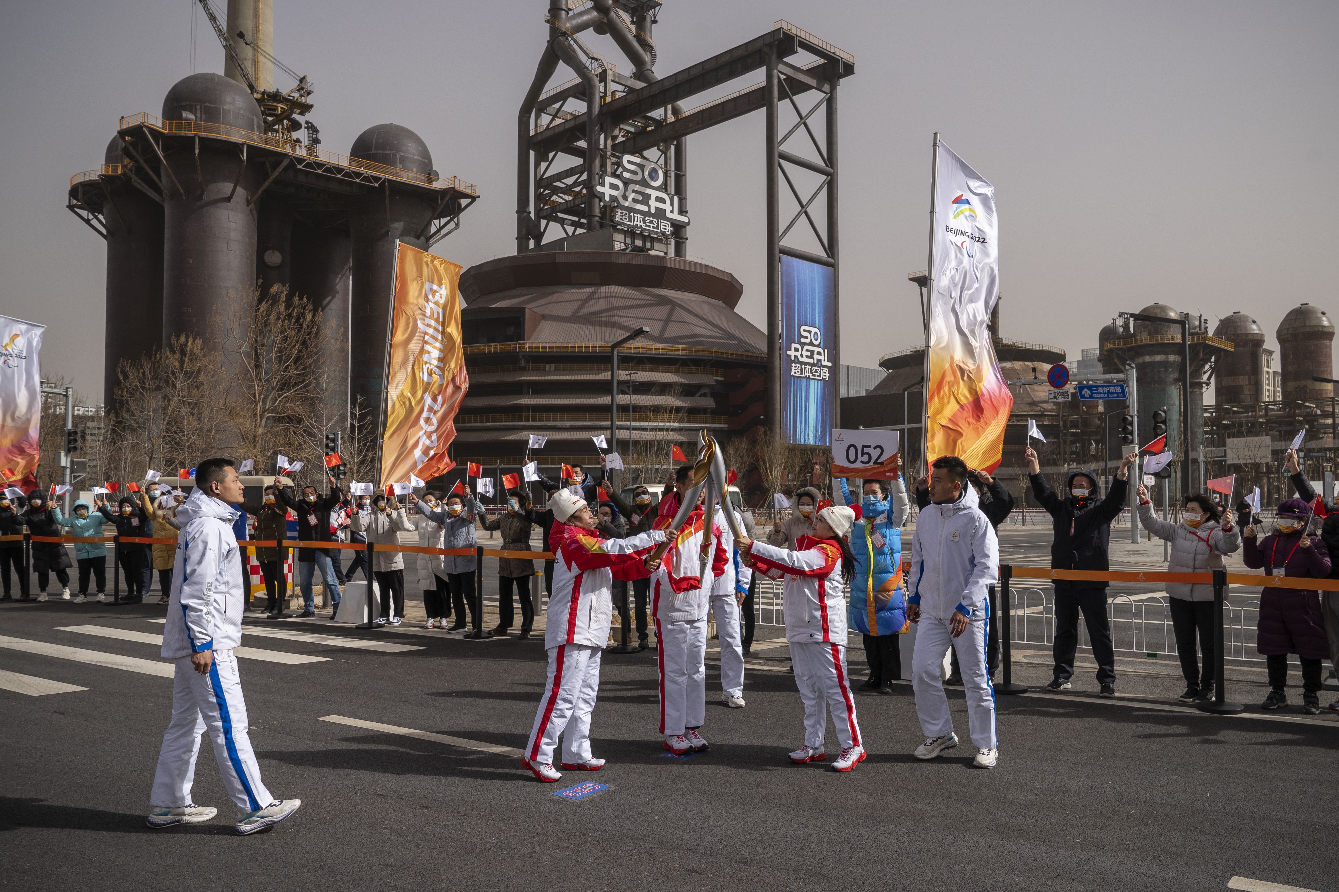 Torch bearers pass the flame to each other during the Beijing 2022 Paralympic torch relay at Shougang Park on March 04, 2022