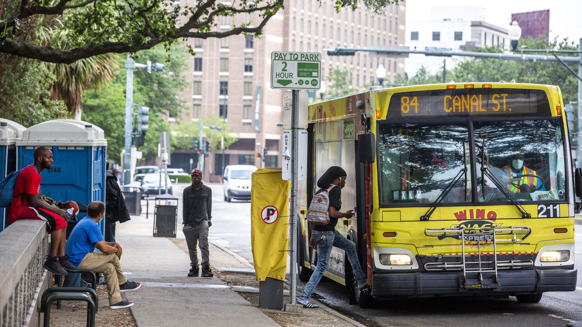 A person climbs aboard a New Orleans public bus on the Canal Street route. Others sit nearby on benches.