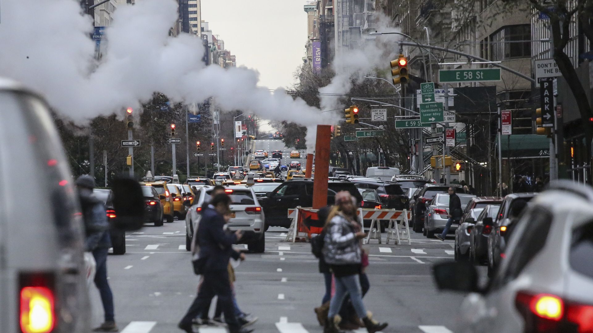 Pedestrians in NYC cross a the street while a pipe emits carbon dioxide emissions 