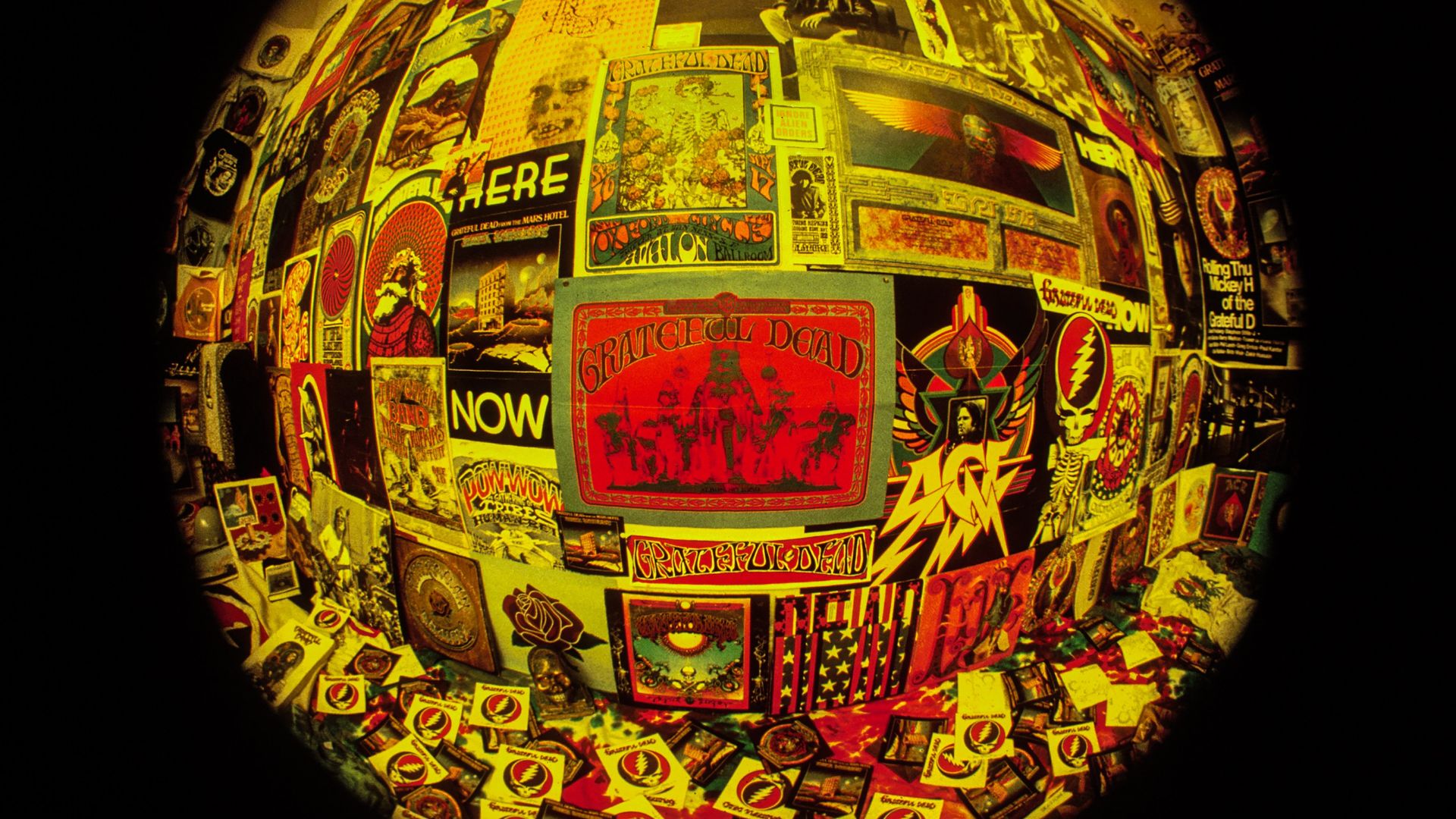 Wall covered with colorful vintage Grateful Dead posters and memorabilia, featuring red, yellow, and black hues, viewed through a fisheye lens creating a circular distortion.