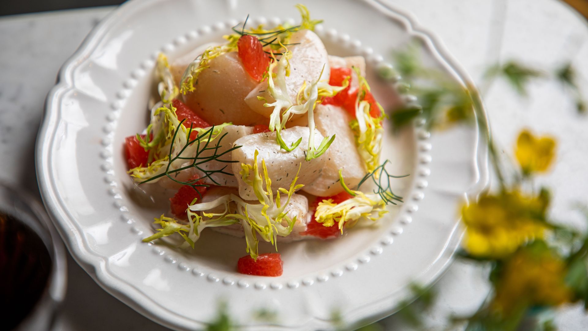 A close-up photo of a white plate with pieces of tuna and fresh herbs.