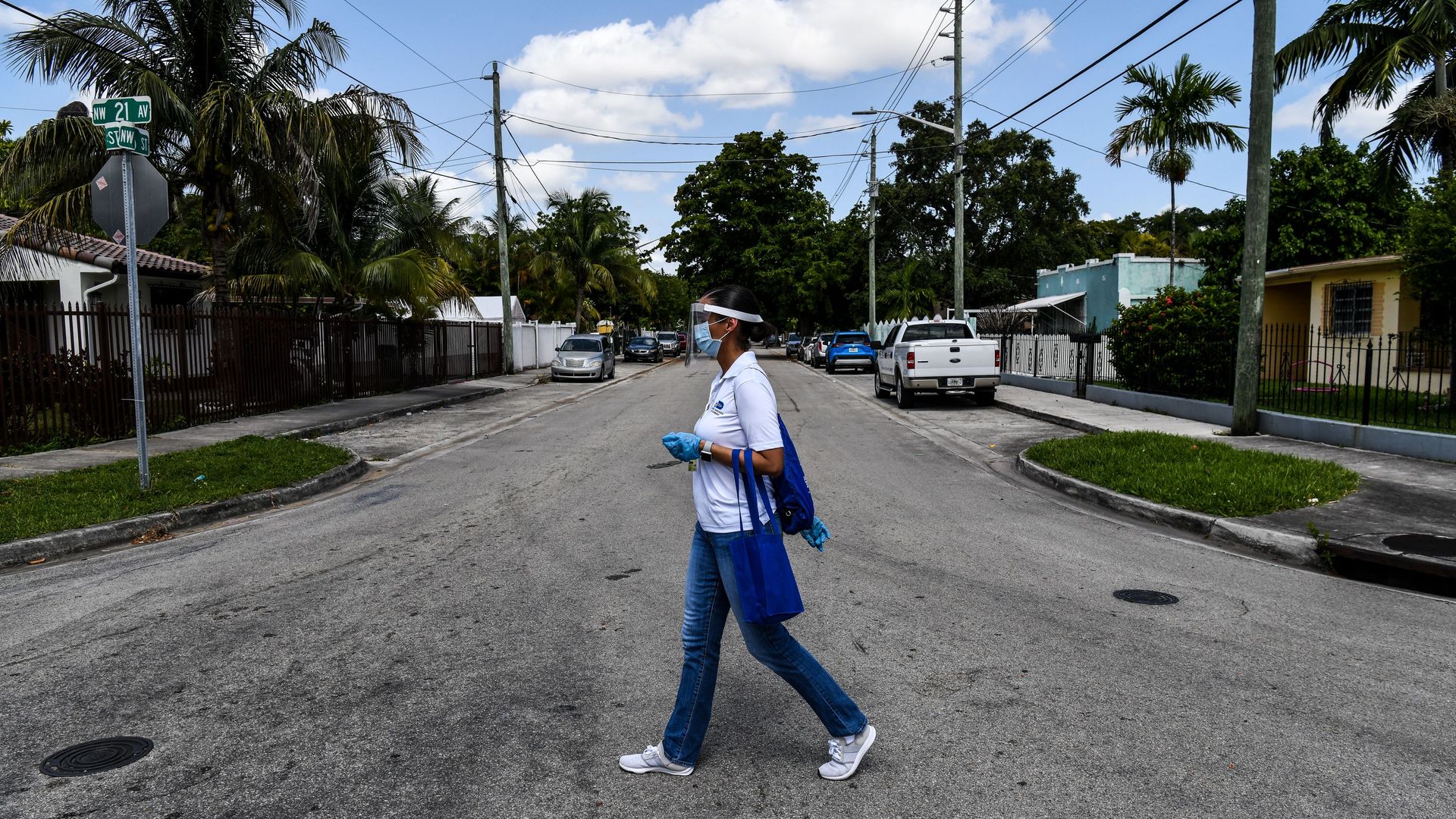 A woman walks across a street while wearing a face mask