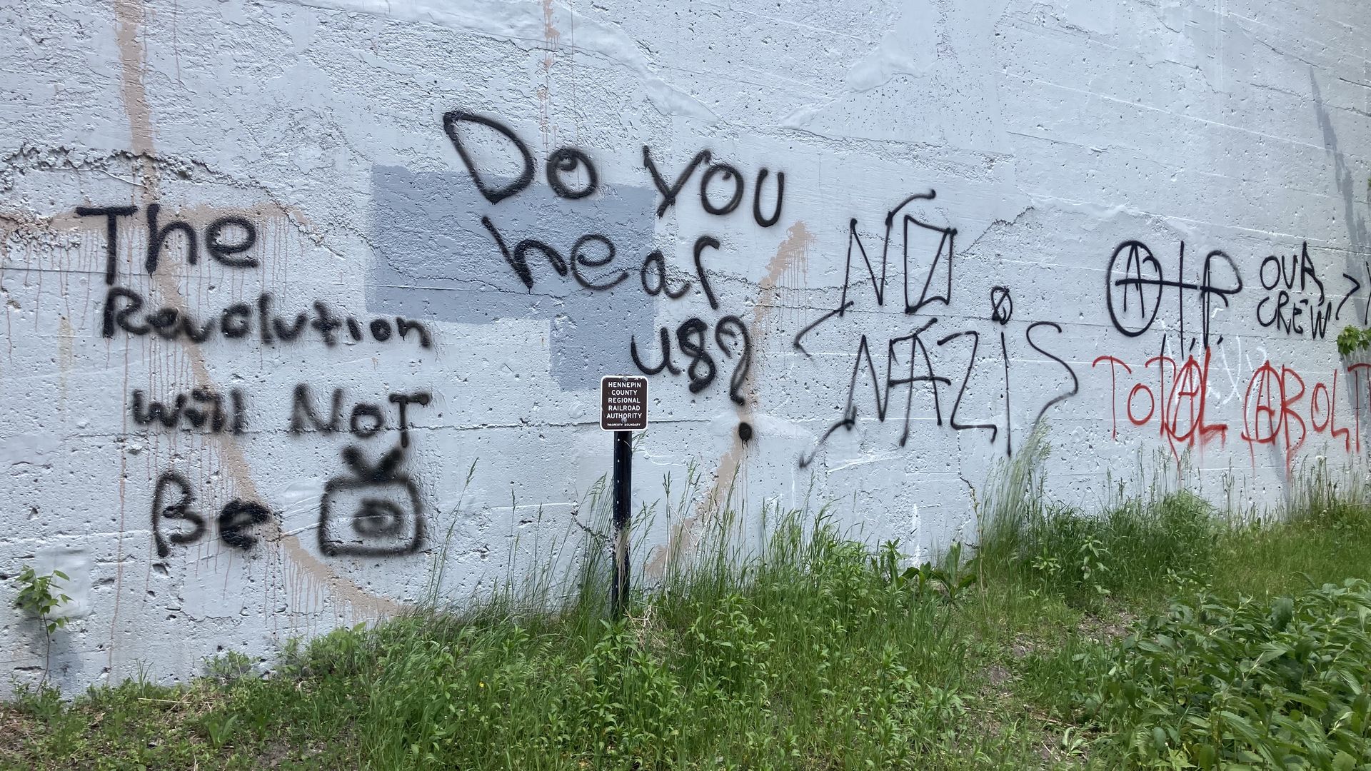 Several political messages are spray painted on a wall in the Midtown Greenway 