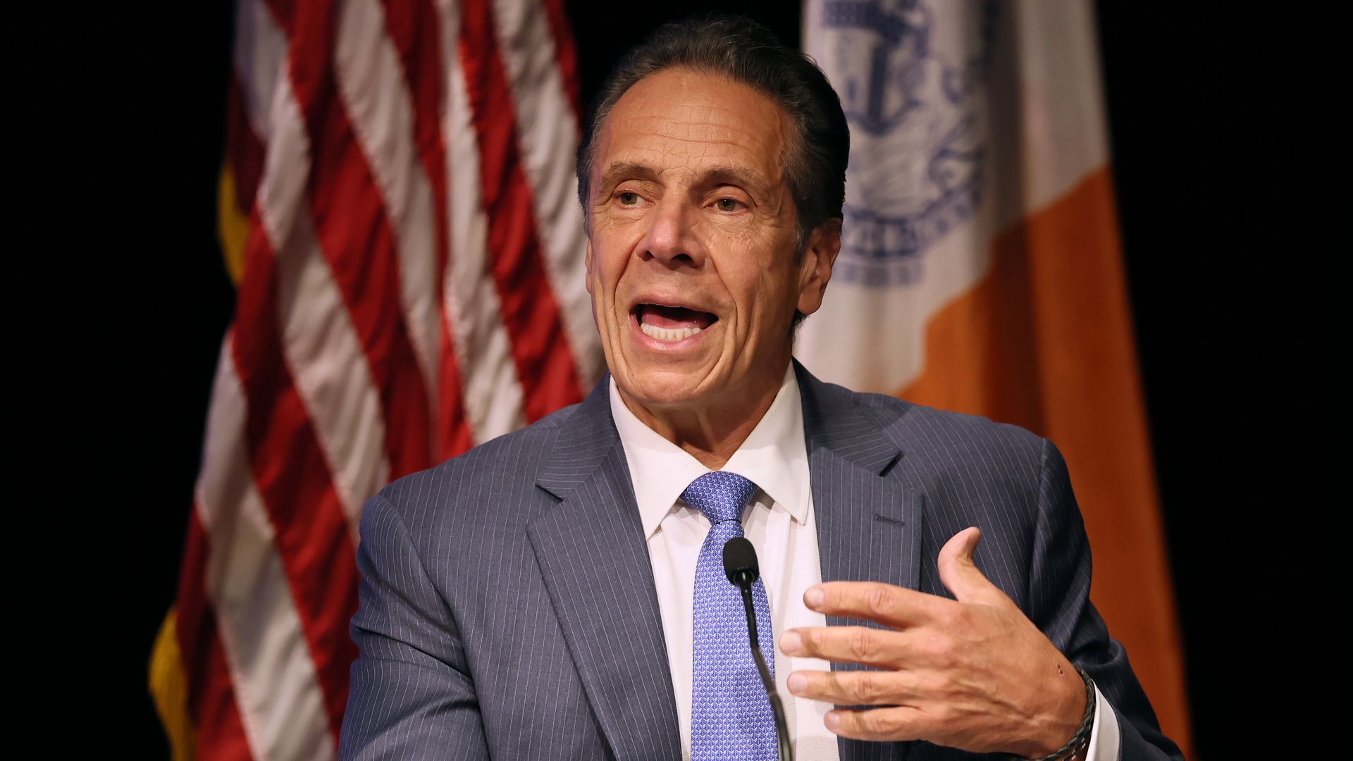 NYC Mayoral Candidate and former Gov. Andrew Cuomo, wearing a gray suit, white shirt and lilac tie with white dots, gestures with his left hand as he speaks into a mic.