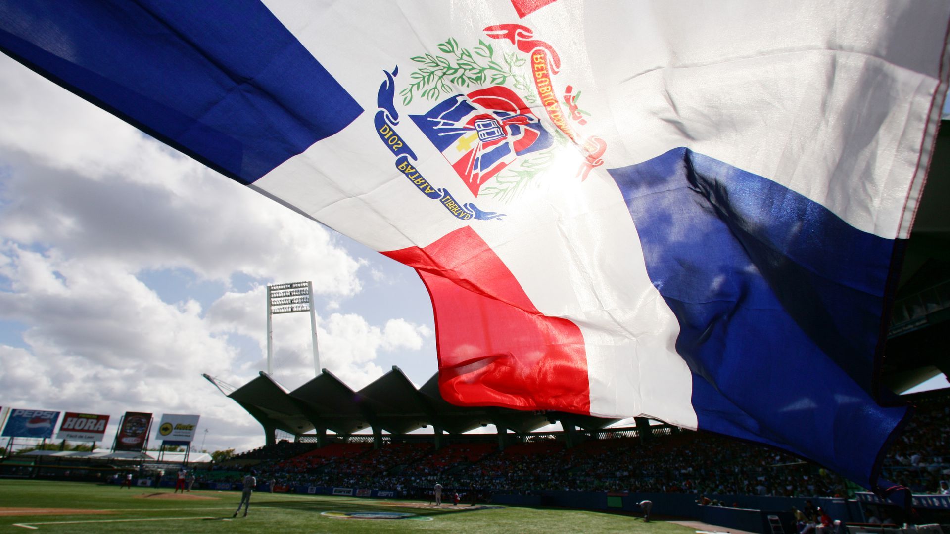 The flag of the Dominican Republic flies over a baseball field.
