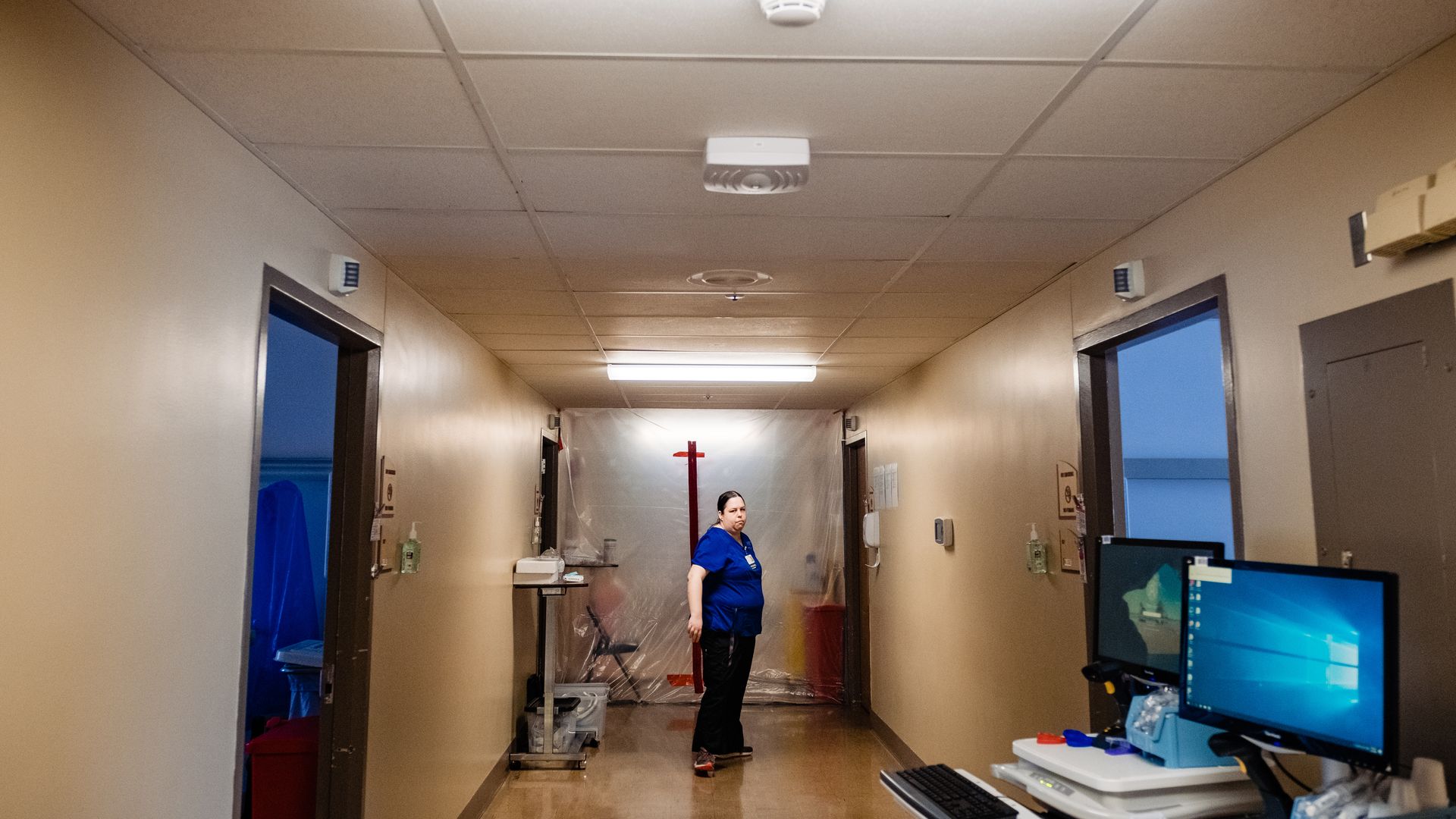 A nurse stands in a hospital hallway with equipment scattered around.