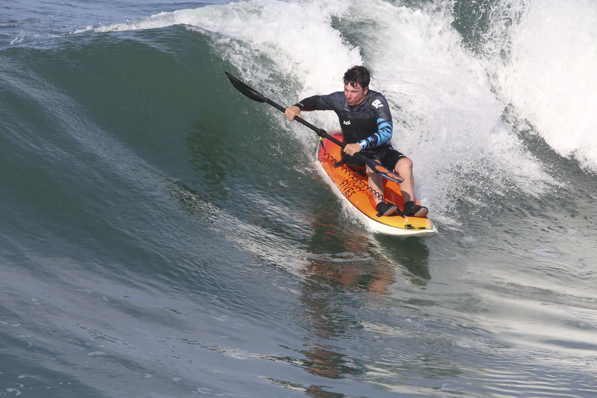 An adaptive surfer rides a wave with a paddle while sitting on a surfboard.