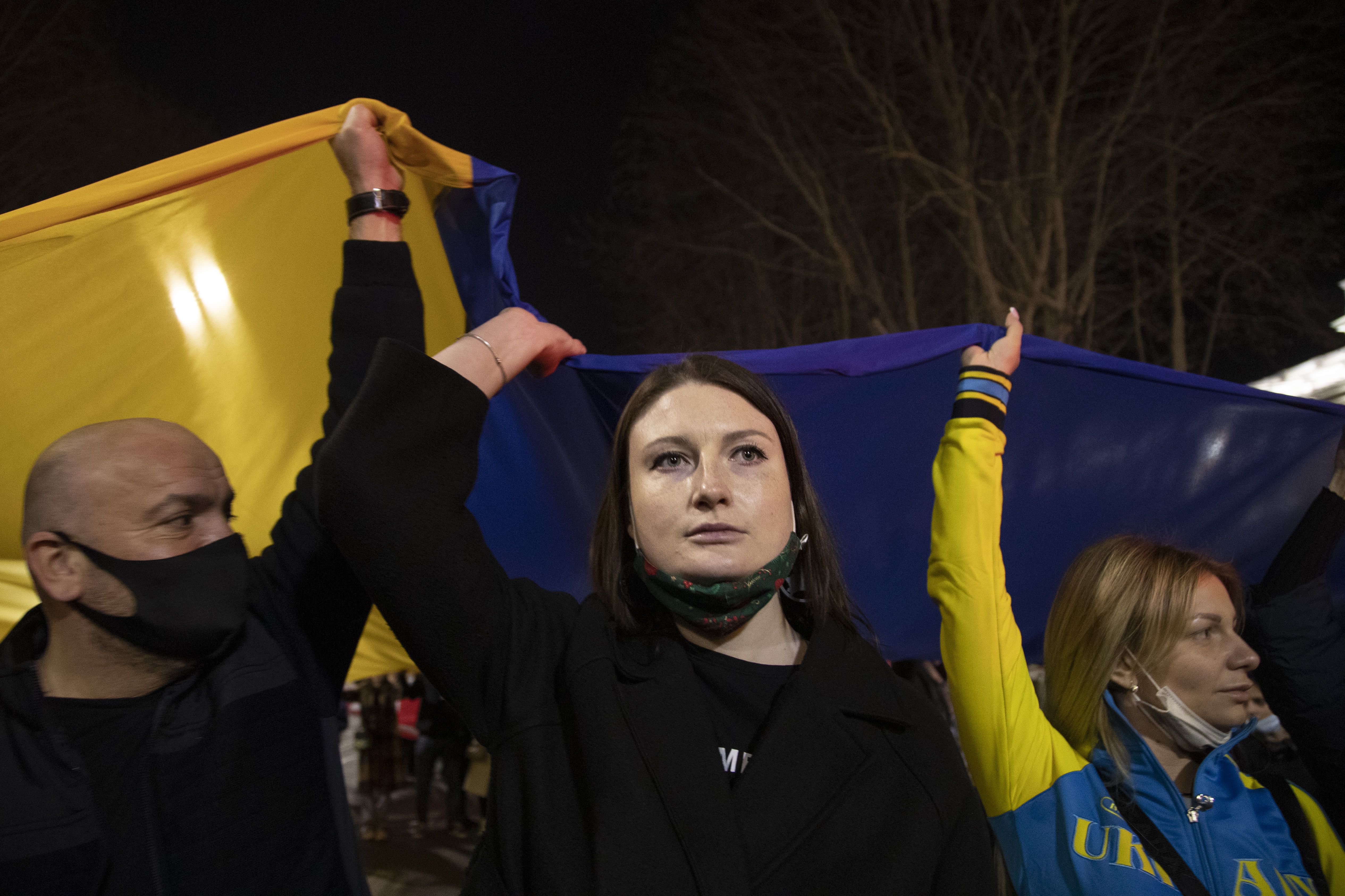 Photo of three people holding a giant Ukraine flag and wearing yellow and blue