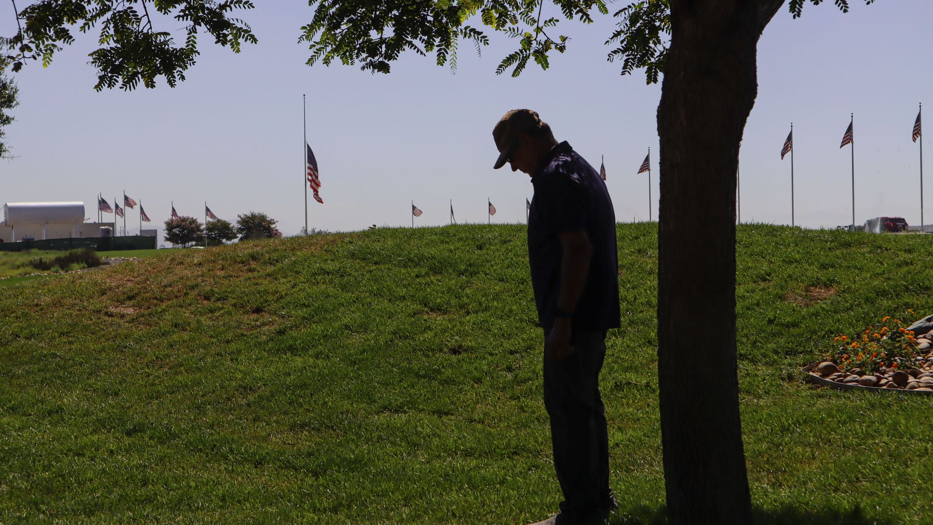 Photo of a man bowing his head next to a tree at a Navy seal memorial ceremony