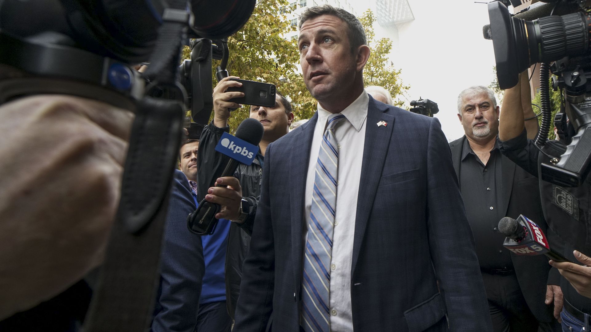 In this image, Duncan walks through a crowd of reporters and TV cameras.