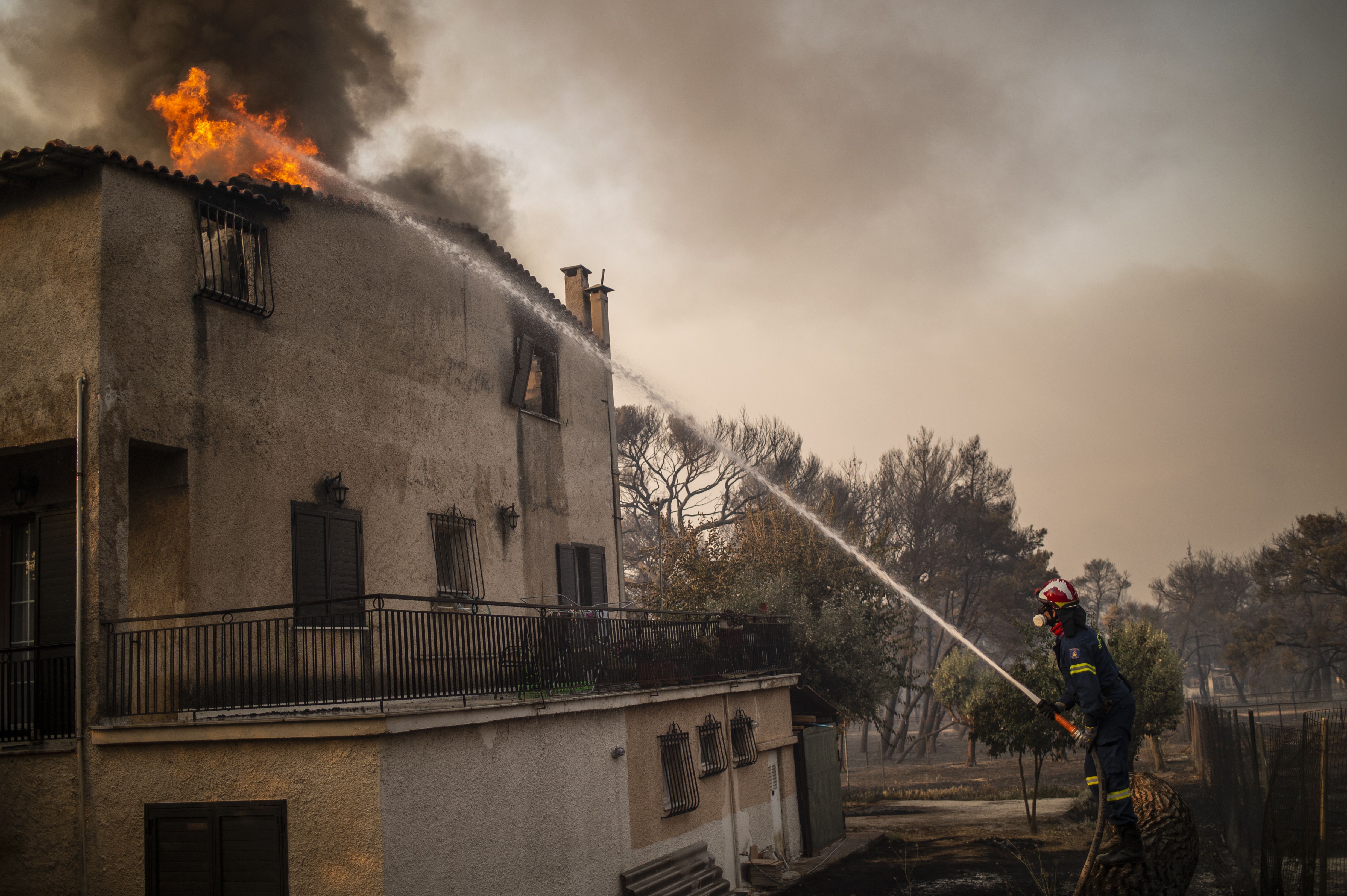 Picture of a house with a fire in the roof and a firefighter with a hose