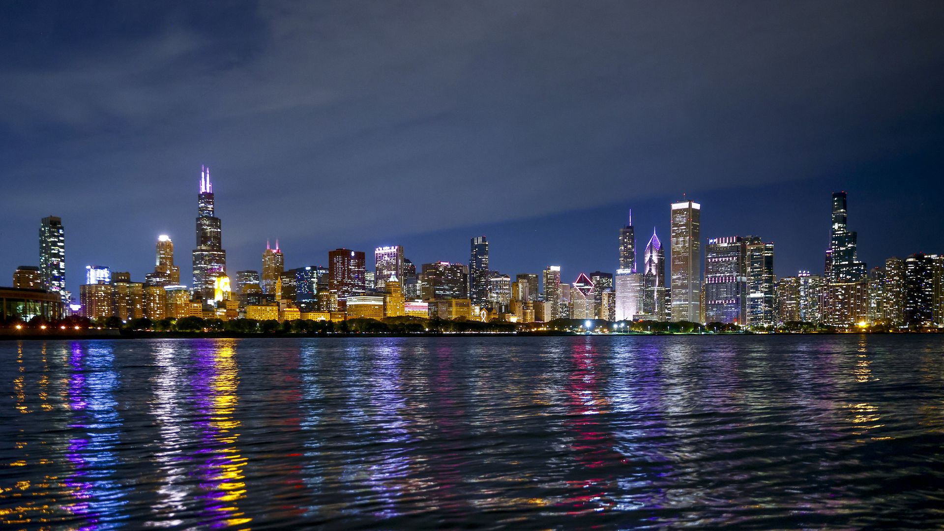 Photo of a skyline of tall buildings at night in front of a body of water