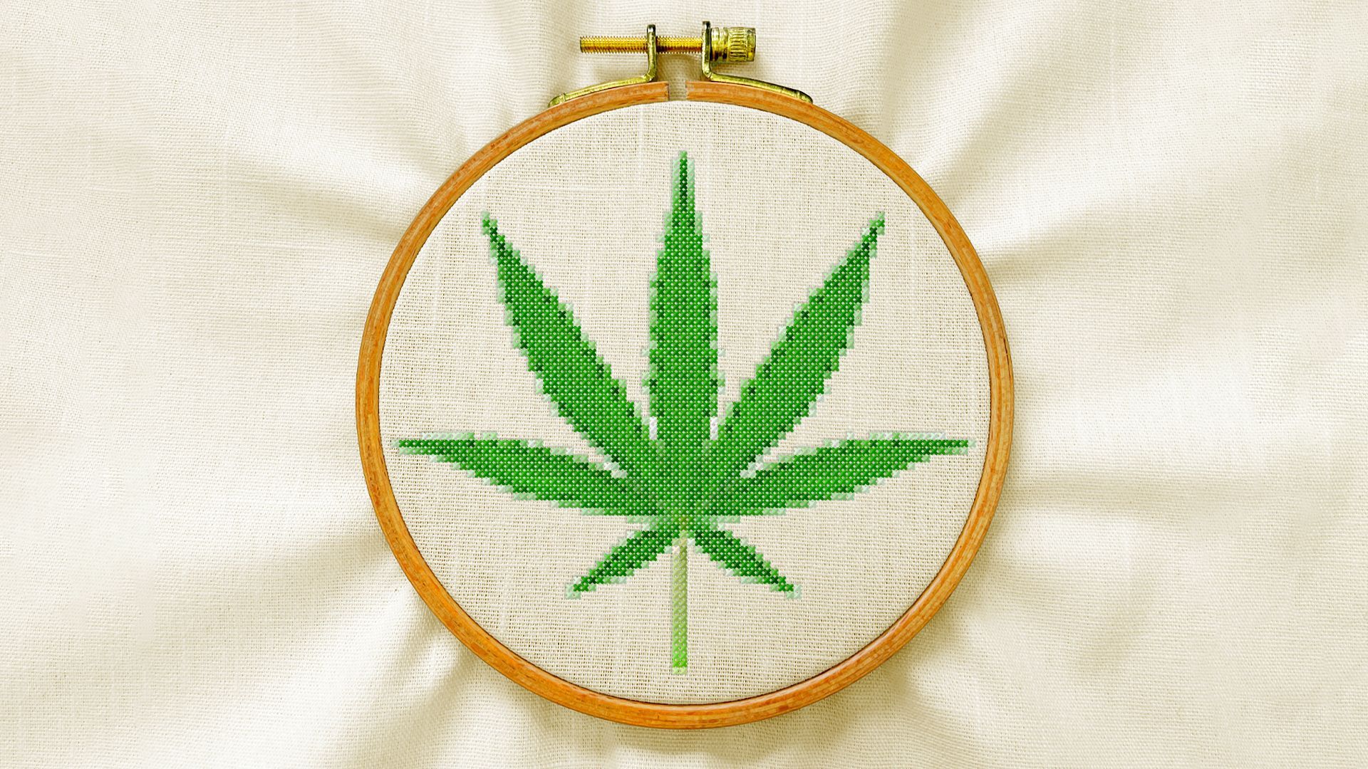 Illustration of an embroidery hoop with a marijuana leaf cross-stitched on linen.