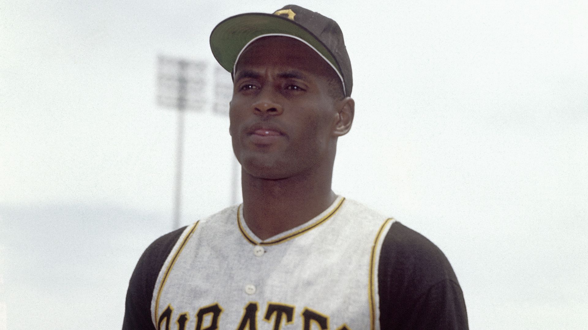 Baseball player wearing a black and white Pittsburgh Pirates jersey with number 21, standing outdoors with a stadium light pole in the background under a cloudy sky.