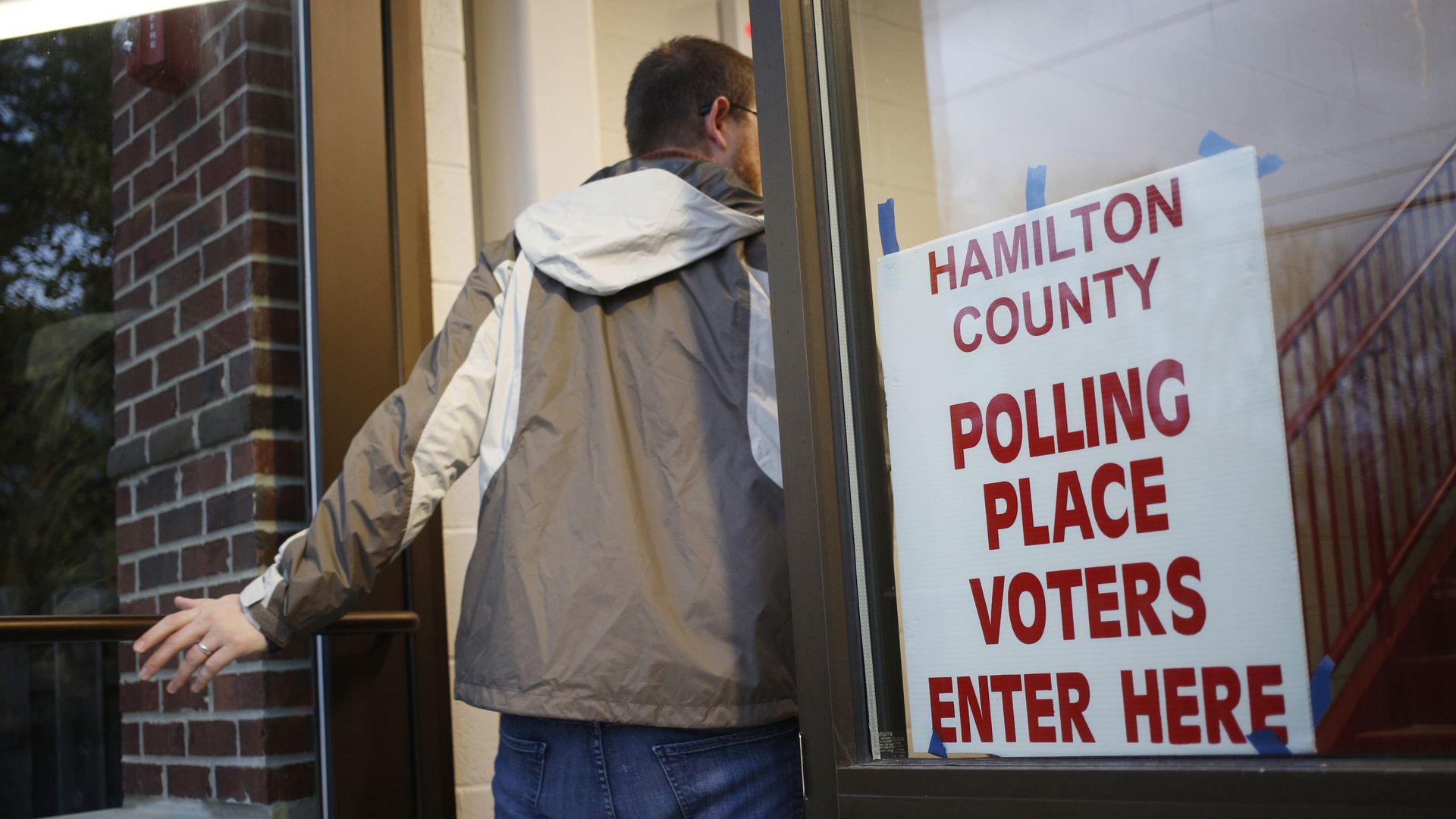 A man wearing a white and beige jacket steps inside a Carmel polling place in pre-dawn light.