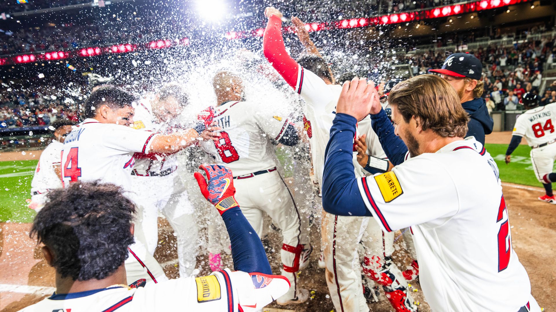 Baseball players wearing white jerseys with red lettering dunk ice and celebrate around a player at home plate.