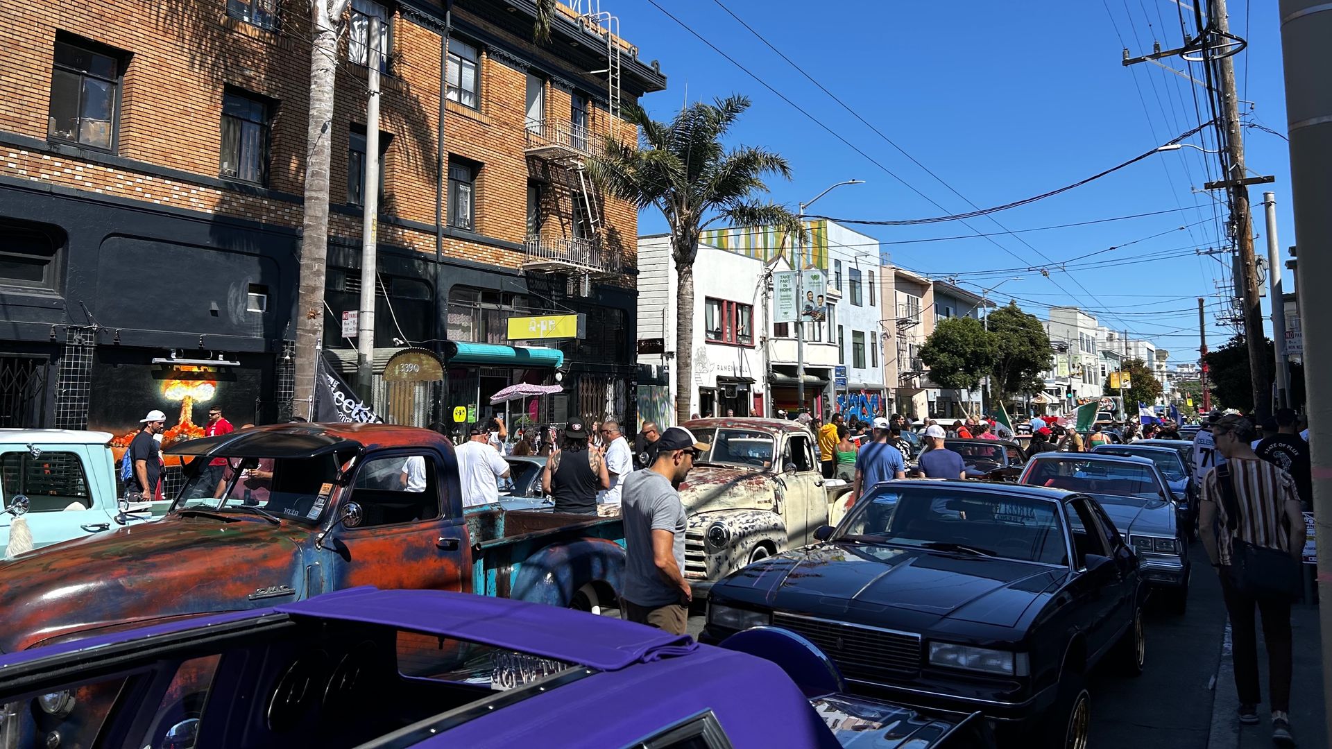 Photo of people crowded into a street filled with parked lowrider cars of all different colors