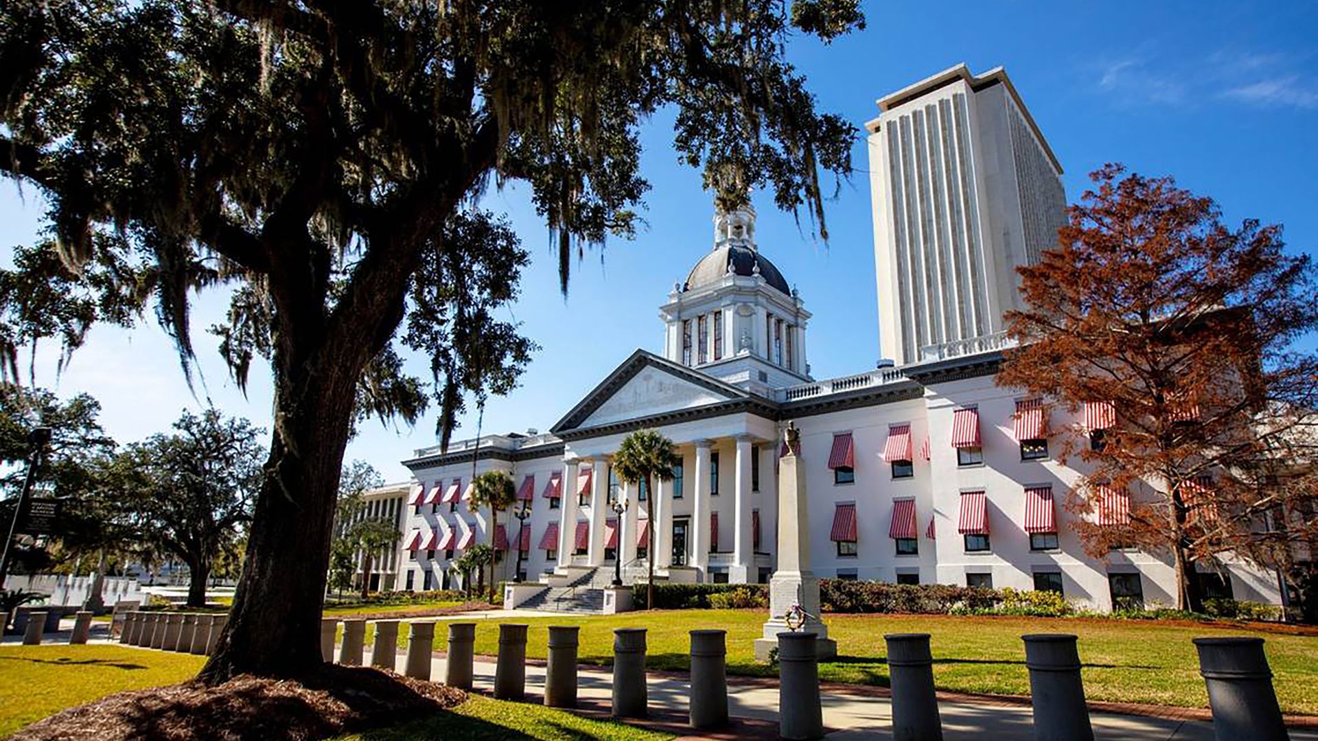 The Old Historic Florida State Capitol building in Tallahassee, a white building with columns and red-and-white awnings over its windows, on a sunny day.