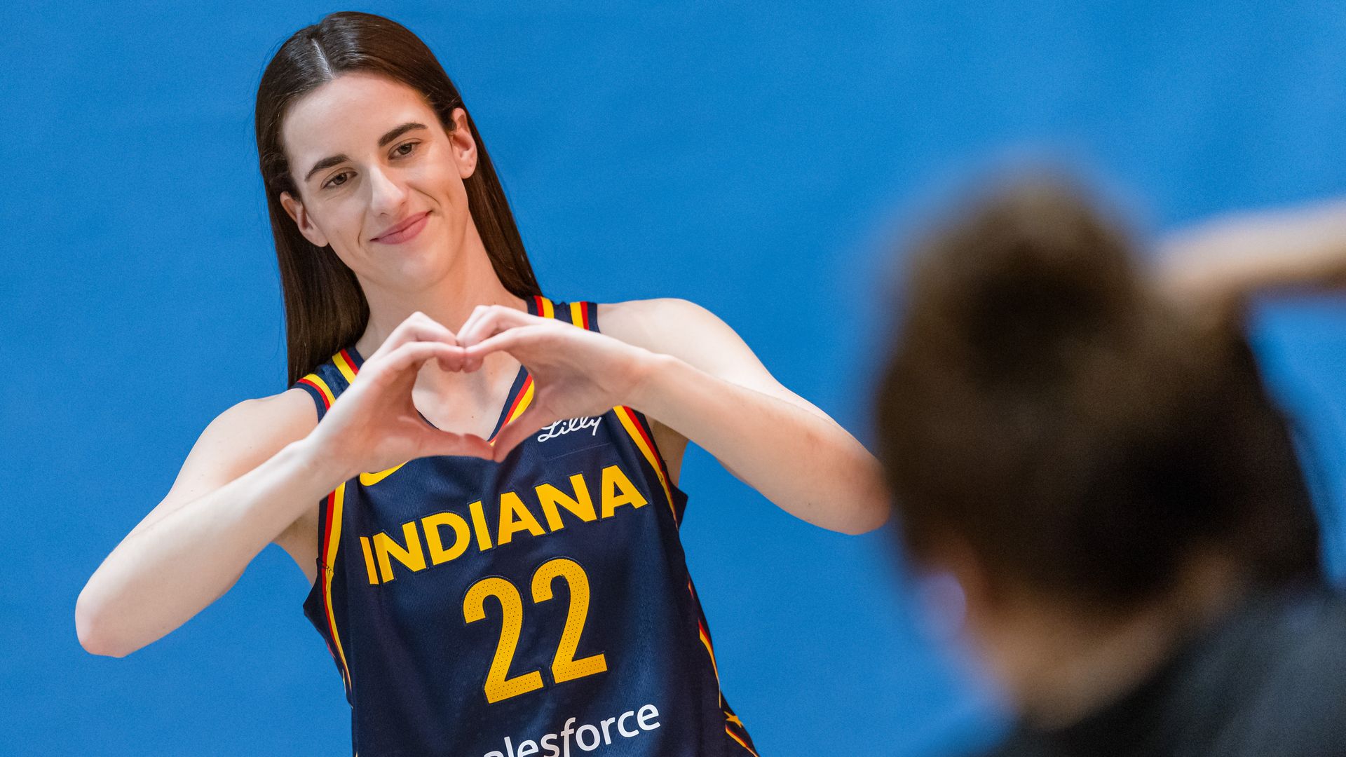 Caitlin Clark does the heart symbol with her hands. 
