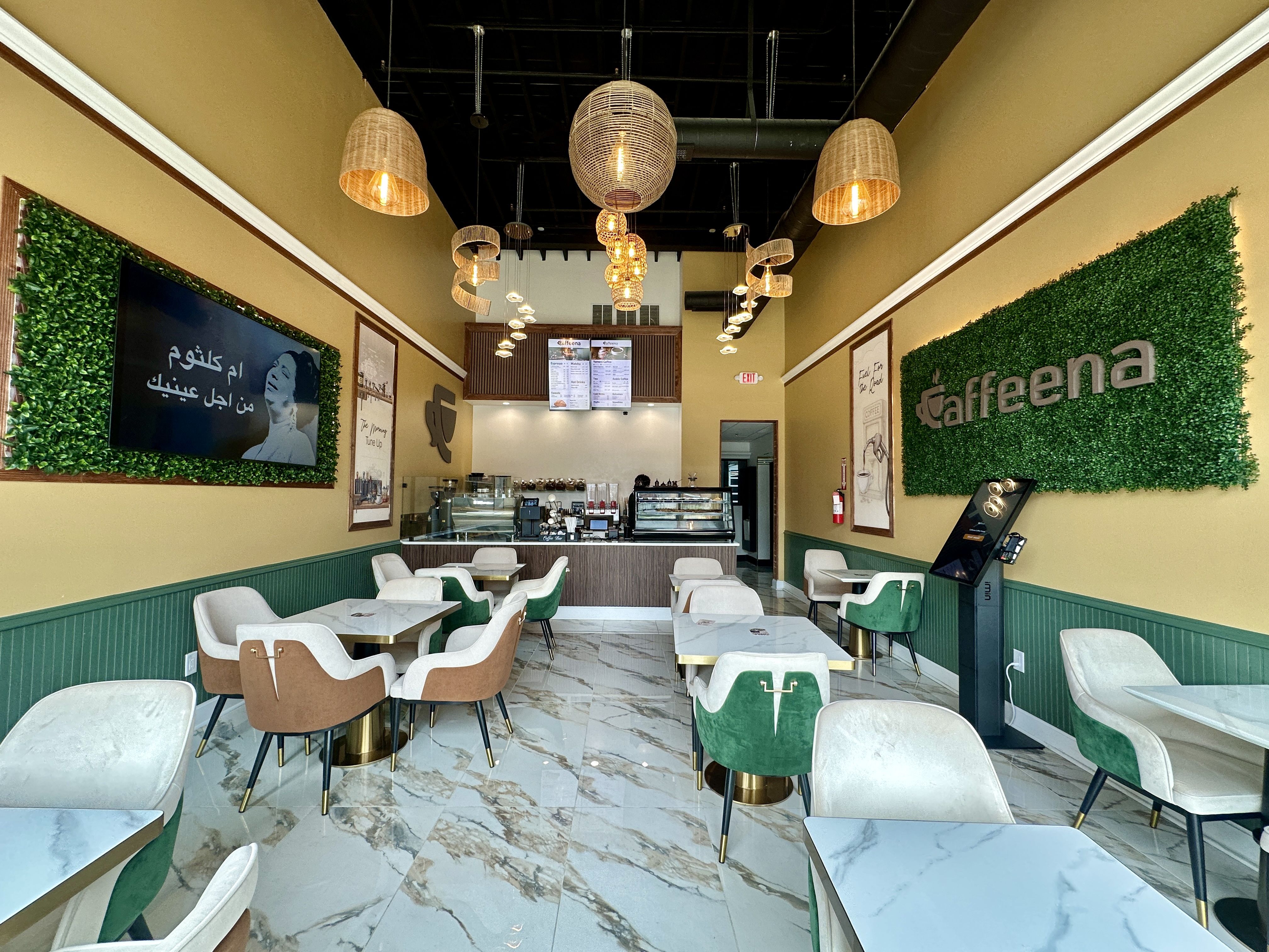 Caffeena CoffeeHouse Charlotte. Inside a bright cafe with yellow walls, green wainscoting, white and green chairs, marble floors, and woven pendant lights hanging from a black ceiling above a counter with a menu board.