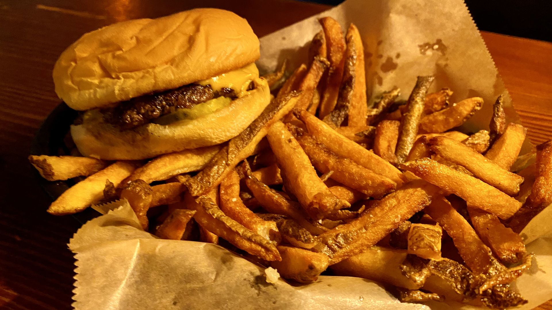 A burger resting on the corner of a basket of fries.