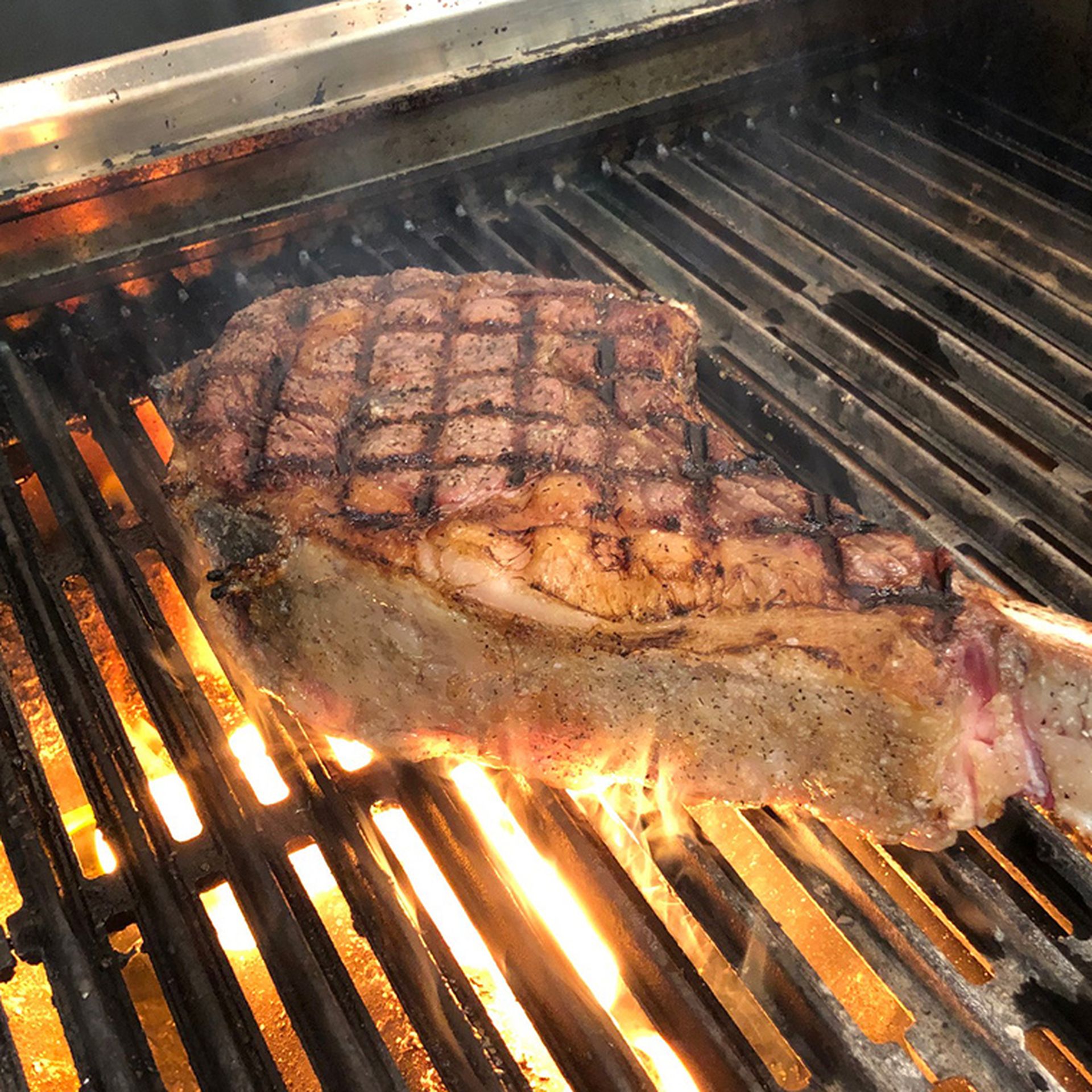 a tomahawk steak over a grill with a flame