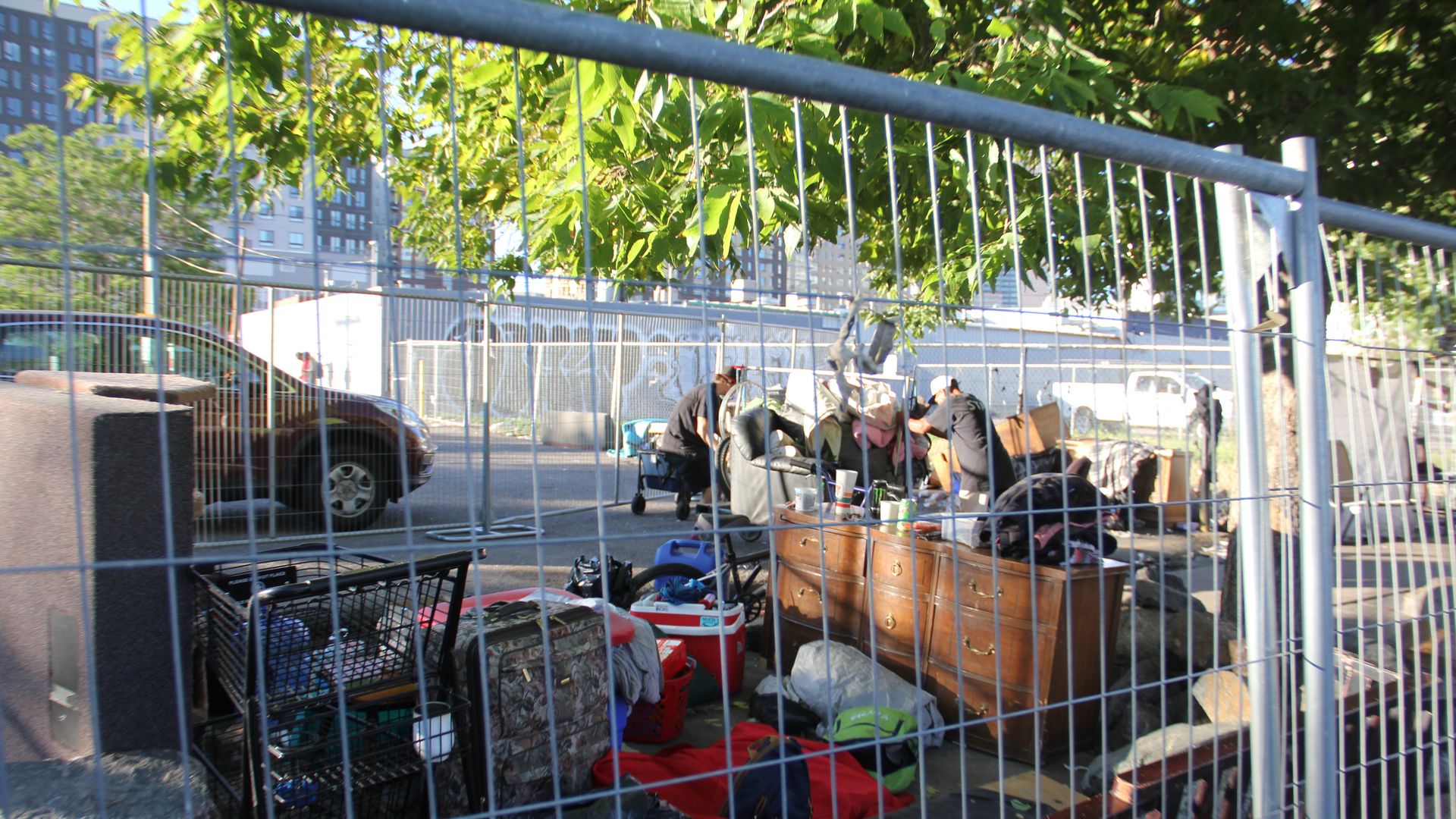 A fence sits in front of a pile of things including clothing inside a homeless encampment. 